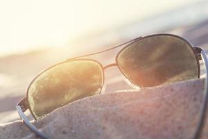 lunettes de soleil sur le sable au coucher du soleil, plage et océan en arrière-plan. photo