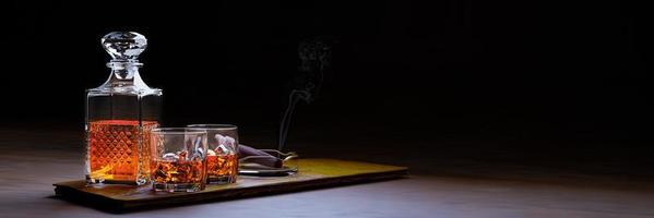 brandy ou whisky dans un verre transparent avec des glaçons. les boissons alcoolisées sont placées sur des sous-verres en bois. concept de boisson au bar cigarettes ou cigares placés dans le cendrier. rendu 3d. photo