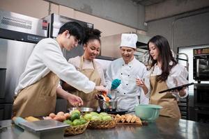 Cours de cuisine passe-temps, chef masculin senior en uniforme de cuisinier enseigne aux jeunes étudiants en cours de cuisine à préparer, mélanger et remuer les ingrédients pour les pâtisseries, les tartes aux fruits dans la cuisine en acier inoxydable du restaurant. photo