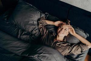 belle jeune fille en pyjama confortable en satin se réveiller en position couchée dans son lit à la maison photo