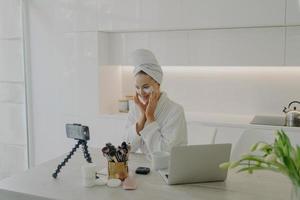 blogueuse beauté féminine en peignoir et serviette sur la tête enregistrant une vidéo sur smartphone pour son vlog photo
