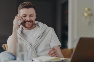 travailleur indépendant souriant parlant au téléphone assis à son bureau au bureau à domicile photo