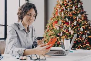 femme d'affaires espagnole détenant une carte de crédit, faisant des achats en ligne sur smartphone pendant la période de noël photo