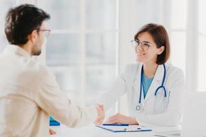 une femme médecin amicale accueille le patient avec une poignée de main, pose dans une clinique privée, s'assoit l'une en face de l'autre, discute, accepte de signer un contrat d'assurance, se rencontre à l'hôpital. concept de soins de santé et de médecine photo