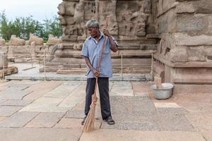 mamallapuram, inde, septembre 2020 - un homme indien âgé balaie le sol en pierre avec un balai de paille des ruines antiques du temple de la rive dans le site du patrimoine de l'unesco de mahabalipuram. photo