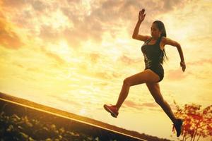 silhouette de jeune femme en cours d'exécution sprint sur route. fit runner fitness runner pendant l'entraînement en plein air avec fond de coucher de soleil. photo