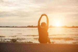 sportif réussi levant les bras sur le ciel doré rétroéclairant le coucher du soleil l'été après la course croisée. athlète masculin de remise en forme avec les bras en l'air célébrant les objectifs après l'exercice de sport et l'entraînement à l'extérieur. photo