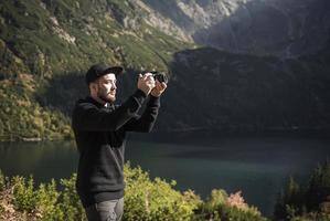 photographe de jeune homme prenant des photos avec un appareil photo numérique dans une montagne.