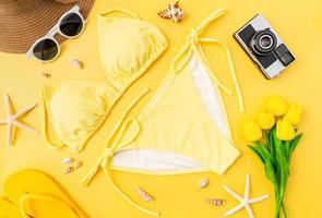 vue de dessus du bikini et des lunettes de soleil avec accessoires de plage sur fond jaune. notion d'heure d'été. photo