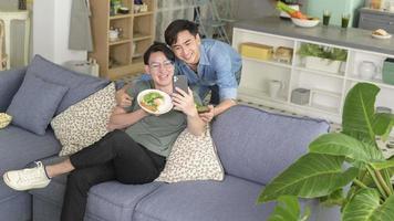 jeune couple gay souriant prenant un selfie avec des aliments sains dans le salon à la maison, lgbtq et concept de diversité. photo