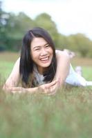 belle femme asiatique en robe blanche se détendre et sourire sur un champ vert dans un parc naturel. une fille thaïlandaise ou une fille chinoise profite des vacances avec la lumière du soleil dans le jardin photo
