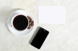 une tasse de café avec des grains de café, un téléphone portable et un blanc vide sur la table photo