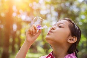 jolie petite fille portant une chemise rose soufflant des bulles dans le parc, style vintage. photo