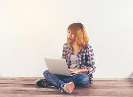 jeune femme hipster assise sur un plancher en bois avec les jambes croisées et utilisant un ordinateur portable sur fond blanc photo
