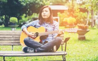 belle jeune femme jouant de la guitare assis sur un banc, concept de temps heureux. photo