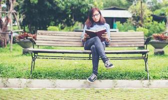 hipster charmante fille se détendre dans le parc tout en lisant un livre, profiter de la nature autour. photo