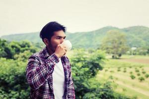 bel homme barbu hipster avec une tasse de café du matin marchant dans le parc. photo