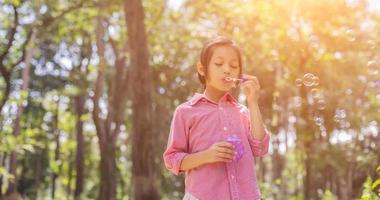 jolie petite fille portant une chemise rose soufflant des bulles dans le parc, style vintage. photo