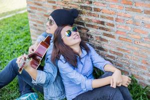 homme hipster jouant de la guitare pour sa petite amie en plein air contre un mur de briques, s'amusant ensemble. photo