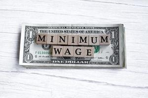 salaire minimum mot écrit sur une cale en bois avec des billets d'un dollar américain. directement au-dessus. photo