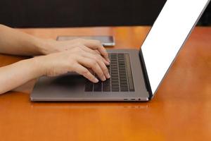 femme tape sur le clavier de l'ordinateur portable assis sur une table près de la fenêtre à la maison. photo