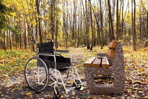 un fauteuil roulant vide garé dans un parc d'automne à côté d'un banc. le concept d'accessibilité des personnes handicapées. photo