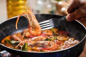 tom yum goong ou tom yum kung, soupe de crevettes aigre-douce thaïlandaise dans une poêle. cuisine thaïlandaise au restaurant de cuisine thaïlandaise. utiliser une fourchette pour soulever les crevettes hors de la poêle. crevettes et épices au lait de coco. fermer photo