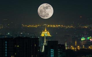 pleine lune surréaliste sur la pagode dorée, point de repère à bangkok, thaïlande, avec vue sur le paysage urbain photo