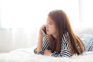 belle jeune femme asiatique souriante allongée se détendre sur le lit le matin, fille à l'aide de téléphone portable intelligent parler profiter, concept de communication et de réseau social. photo