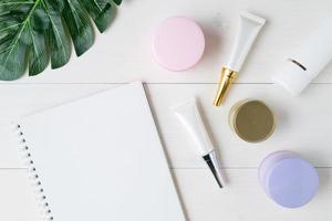 produit cosmétique et de soin de la peau et carnet et feuilles sur la table, beauté avec crème de traitement et hydratant et espace de copie du bloc-notes sur le bureau en bois, concept de santé et de bien-être, vue de dessus. photo