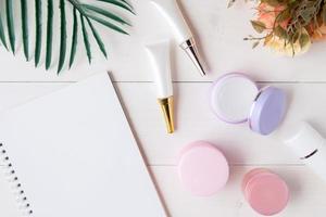 produit cosmétique et de soin de la peau et carnet et feuilles sur la table, beauté avec crème de traitement et hydratant et espace de copie du bloc-notes sur le bureau en bois, concept de santé et de bien-être, vue de dessus. photo