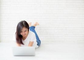 jeune femme asiatique travaillant sur un ordinateur portable en ligne allongé sur fond de ciment de brique au sol, fille indépendante utilisant un ordinateur portable avec connexion à internet pour le travail à distance, les affaires et le concept de style de vie. photo