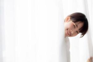 portrait d'une belle jeune femme asiatique debout à la fenêtre et souriant tout en se réveillant avec le lever du soleil le matin, fille heureuse avec fraîcheur et gaieté, mode de vie et concept de détente. photo