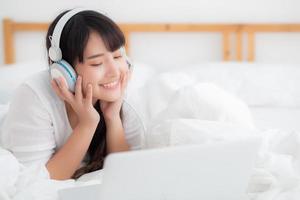 belle jeune femme asiatique allongée dans la chambre à l'aide d'un ordinateur portable montrant un chat par appel vidéo à la maison, une fille salue et écoute et parle le messager, la communication et le concept de style de vie. photo