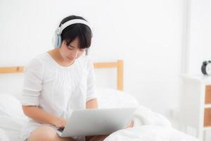 belle jeune femme asiatique allongée dans la chambre à l'aide d'un ordinateur portable montrant un chat par appel vidéo à la maison, une fille salue et écoute et parle le messager, la communication et le concept de style de vie. photo