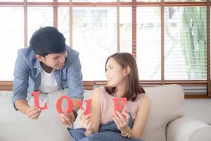 beau jeune couple asiatique assis sur un canapé tenant le mot amour ensemble dans le salon, famille mari et femme souriant avec heureux, homme et femme amoureux portant décontracté avec détente, concept de style de vie. photo