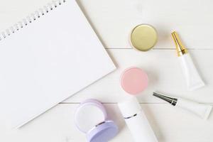 produit cosmétique et de soin de la peau et cahier sur table en bois blanc, beauté avec crème de traitement et hydratant et espace de copie du bloc-notes sur un bureau en bois, concept de santé et de bien-être, vue de dessus. photo