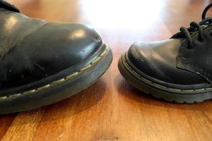 Grande et petite vieille chaussure en cuir noir sur un plancher en bois photo