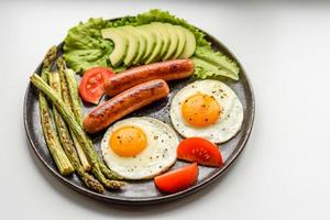 un délicieux petit-déjeuner nourrissant avec des œufs au plat, des saucisses, des asperges, des tomates, de l'avocat, des épices et des herbes photo