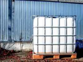 réservoir d'eau carré blanc avec récipient à grille métallique pour liquide debout à l'extérieur sur une palette en bois devant un mur en acier photo