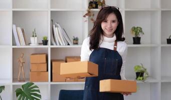 démarrage PME petite entreprise entrepreneur PME ou femme asiatique indépendante utilisant un ordinateur portable avec boîte, jeune femme asiatique réussie avec sa main levée, boîte d'emballage de marketing en ligne et livraison, concept PME. photo