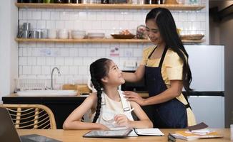 mère et enfant asiatique petite fille apprenant et regardant un ordinateur portable faisant ses devoirs étudiant les connaissances avec le système d'apprentissage en ligne de l'éducation en ligne. conférence vidéo pour enfants avec enseignant tuteur à la maison photo