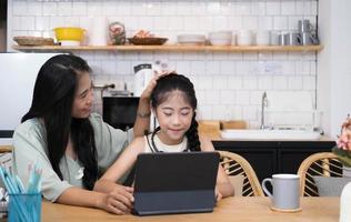 mère et enfant asiatique petite fille apprenant et regardant un ordinateur portable faisant ses devoirs en étudiant avec le système d'apprentissage en ligne de l'éducation en ligne. conférence vidéo pour enfants avec un enseignant tuteur à la maison photo