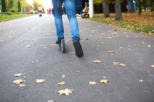 les jambes d'un homme en jeans et baskets sur un scooter dans le parc en automne avec des feuilles jaunes sèches tombées sur l'asphalte. balades d'automne, mode de vie actif, transports écologiques, circulation photo