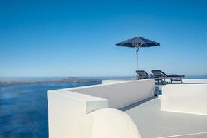 toit blanc avec terrasse, destination lune de miel romantique. rêve d'amour voyageant dans la ville d'oia sur l'île de santorin. voyage romantique d'été en vacances, chaises sous parapluie. vacances luxueuses photo