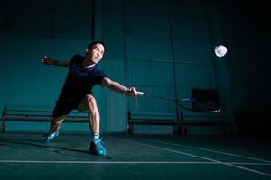 un joueur de badminton professionnel utilise une raquette frappée un coq ou un volant sur le terrain pendant l'échauffement avant la compétition du tournoi en homme seul sur un court intérieur photo