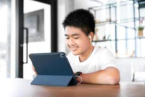 un étudiant asiatique heureux garçon porte un casque et étudie en ligne avec un appel vidéo enseigné par un enseignant avec une tablette intelligente et un ordinateur portable de la maison pendant le covid-19