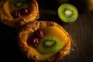 tarte aux fruits avec kiwi, cerise, kaki, posé sur une bande d'acier sur le banc en bois à fond noir photo