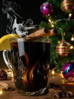 boisson chaude alcool, vin rouge chaud dans une tasse de verre épices bâton de cannelle et agrumes. sapin décoré festif sur table en bois. célébration noël et bonne année concept. photo