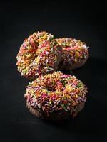 trois beignets glacés avec des pépites colorées isolées sur fond noir. vue d'ange. photo